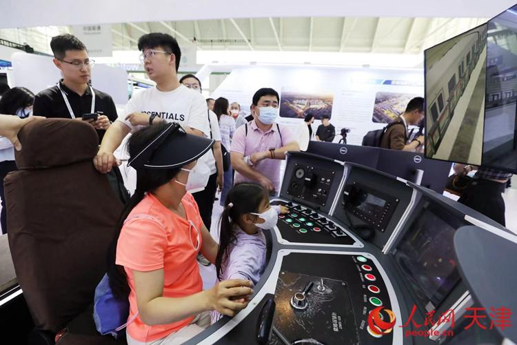 一位參觀者和孩子在天津軌道交通集團展臺體驗智能駕駛帶來的樂趣。人民網(wǎng)記者 孫翼飛攝